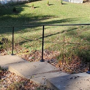A black railing is sitting on top of a concrete walkway next to a grassy field.