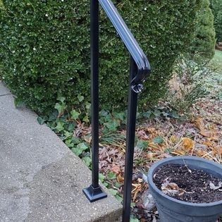 A black railing is sitting on a sidewalk next to a potted plant.