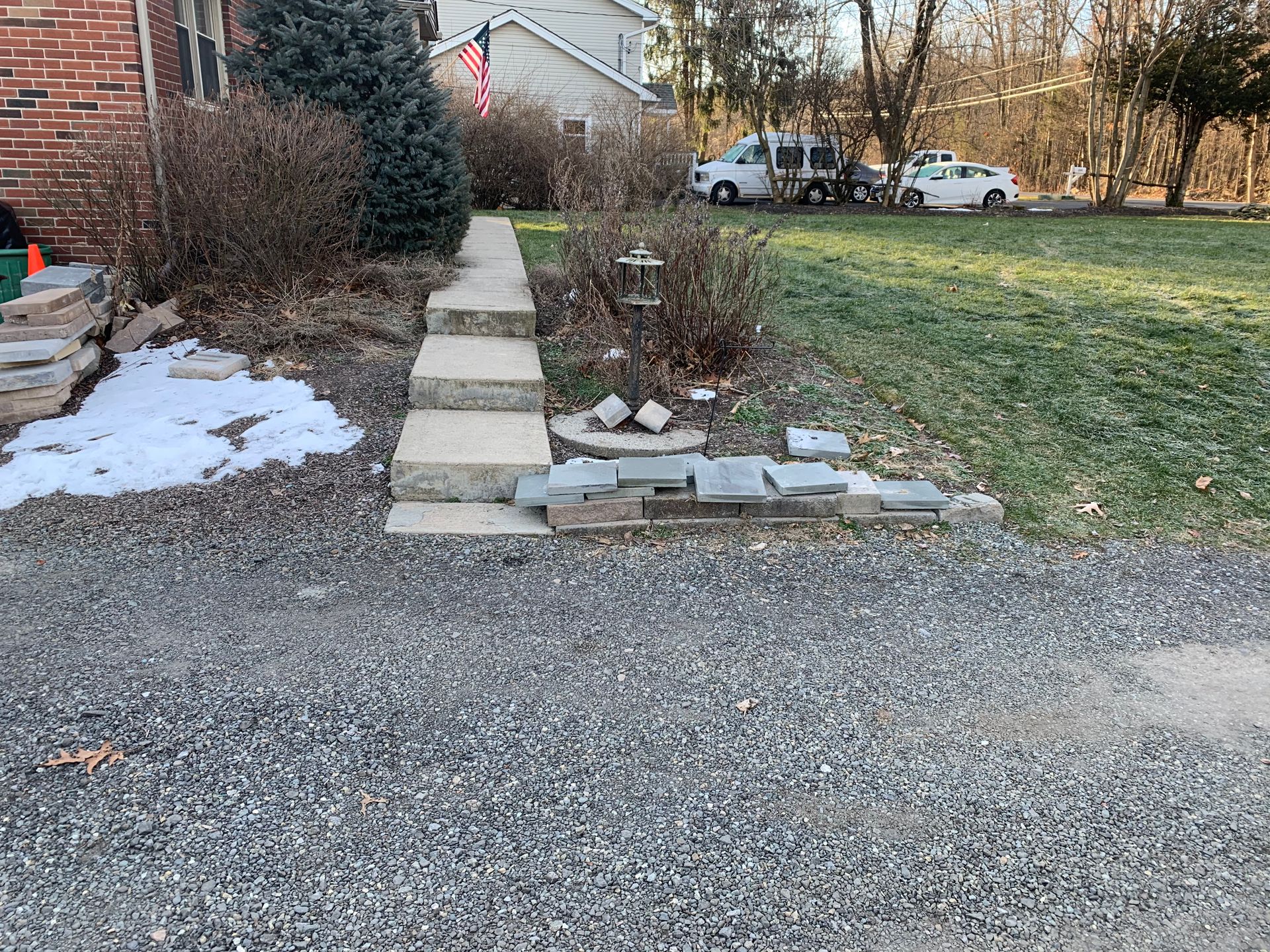 Stone retaining wall in a grassy area with some patches of bare soil, surrounded by greenery.