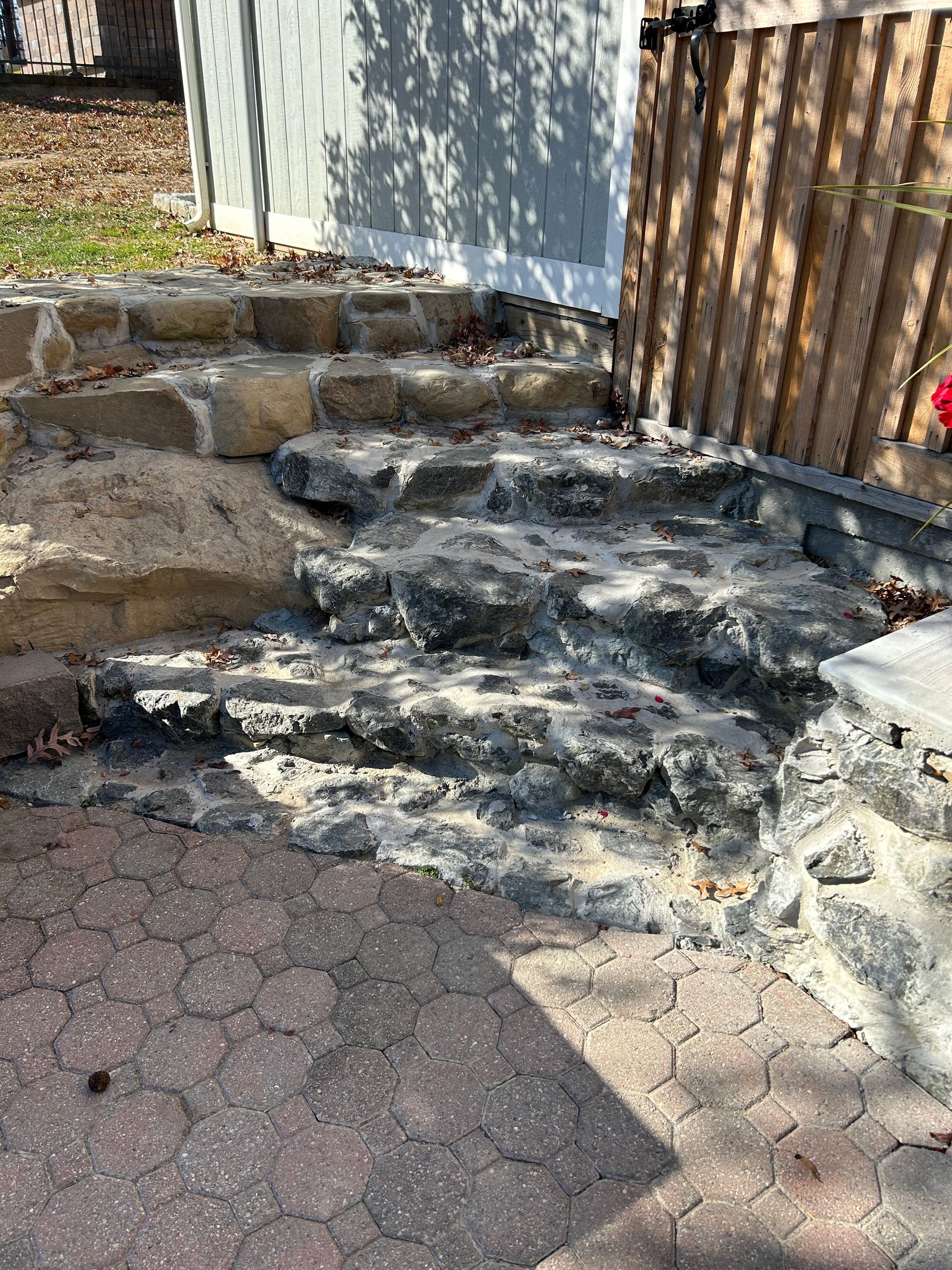 Backyard with a brown retaining wall, white fence, and a diving board near a dried pool area under a cloudy sky.