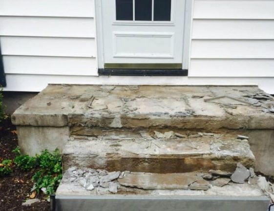 Damaged concrete steps in front of a white door and siding. Chipped and crumbling steps.