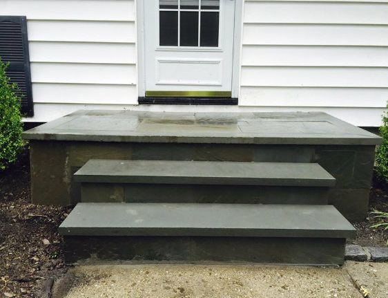 Stone steps lead up to a white door, set against a white siding house.