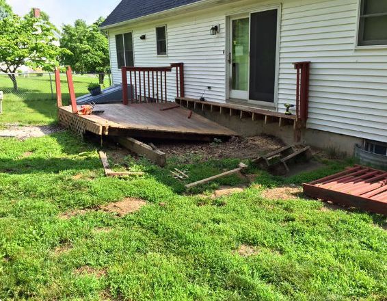 Damaged deck attached to a white house, with visible wood rot and debris on the ground.