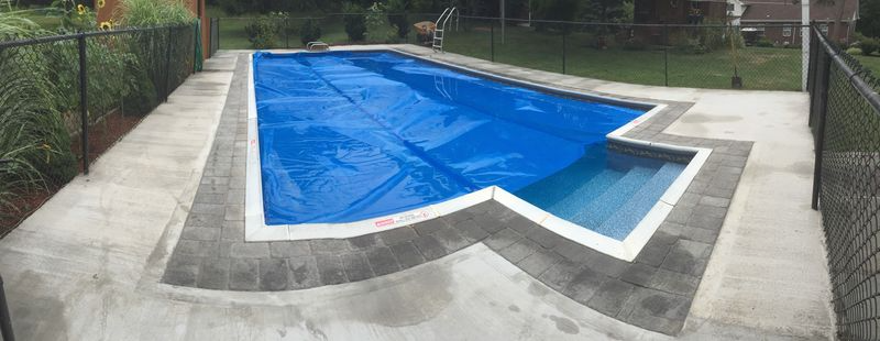 A rectangular pool covered with a blue tarp, surrounded by a concrete patio and a black fence.