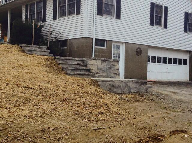 House exterior with steps and a garage. Tan ground with mulch and concrete steps. White siding.