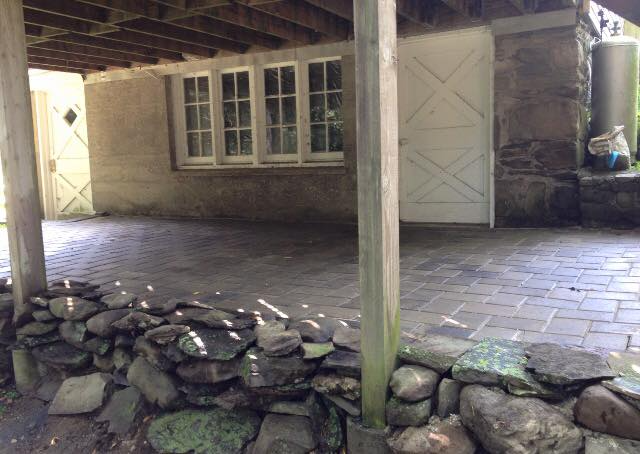 Covered patio with stone wall and brick paving, building with white doors and windows.