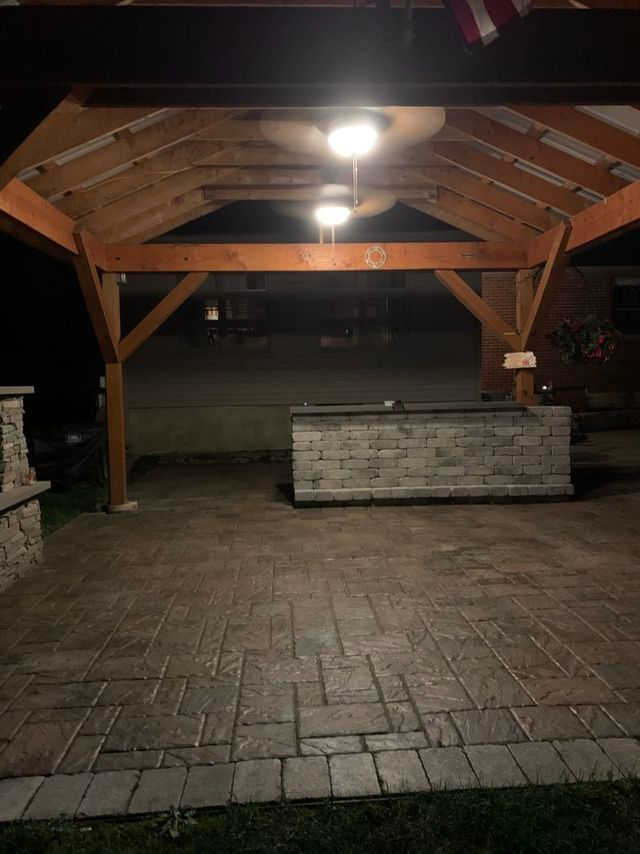 Patio under a wooden pergola at night, with a brick structure and stamped concrete.
