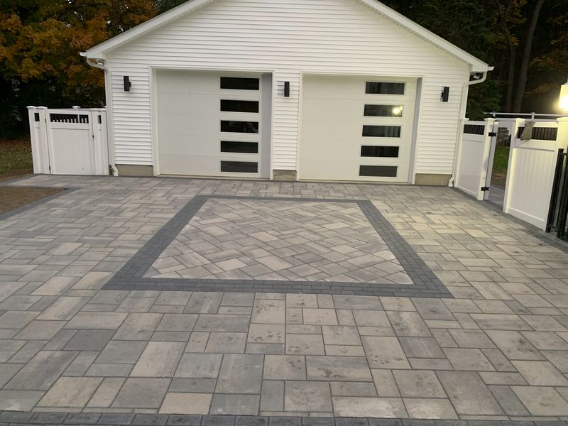 Paved driveway in front of a white garage with modern doors. A gray square is in the center with a darker border.