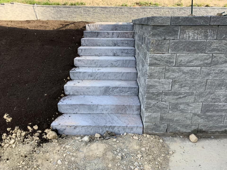 Stone steps leading up, next to a retaining wall made of gray blocks; dirt and landscaping.