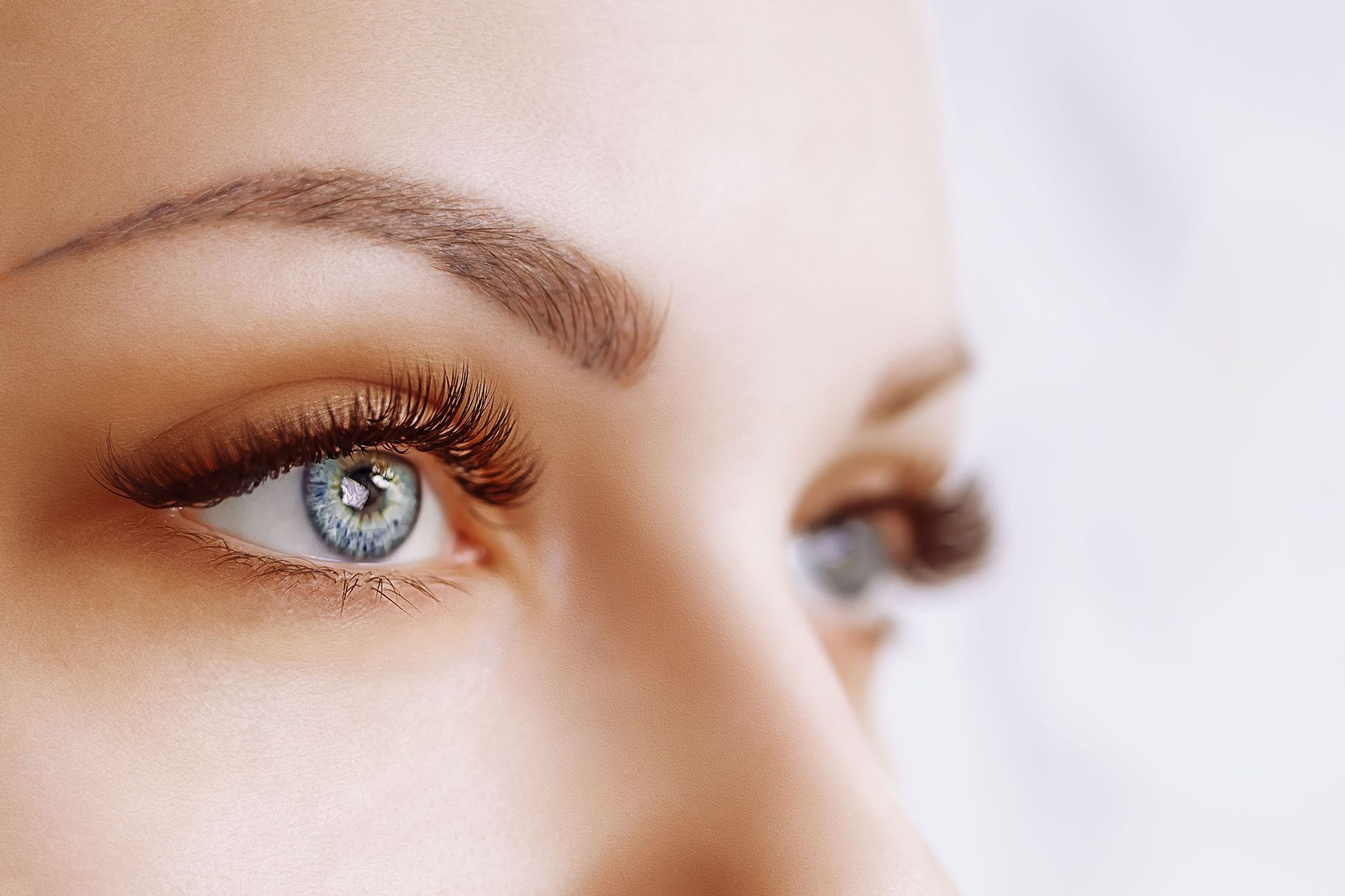 Close-up of a person's light blue eyes with dark lashes and brown eyebrows.