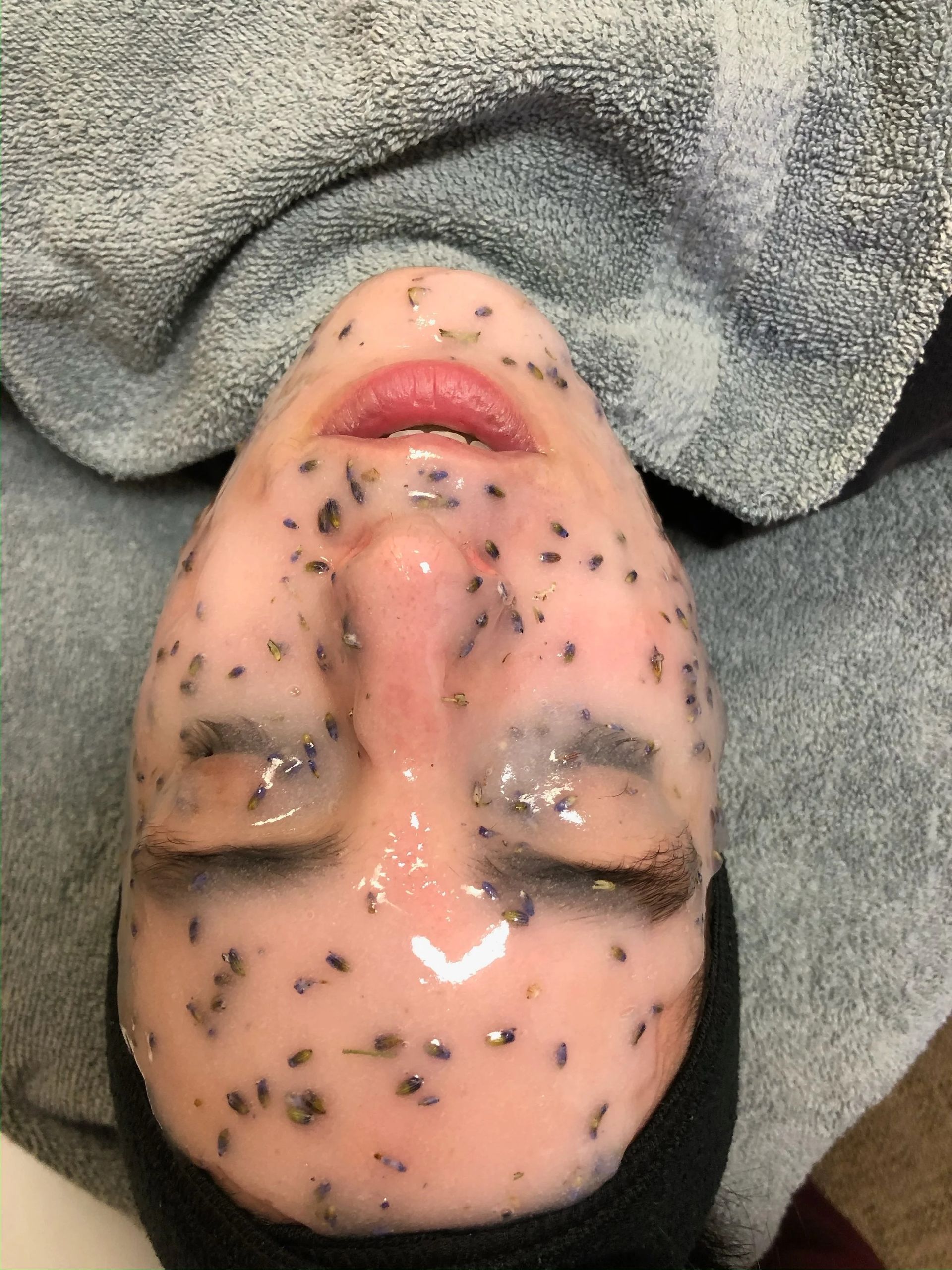 Face covered in a pinkish gel with dark specks; eyes closed, resting on a towel.