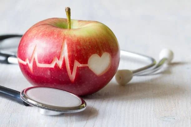 Red apple with heart and EKG carving, next to a stethoscope.