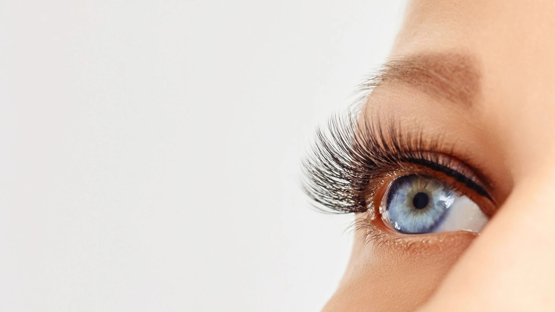 Close-up of a blue eye with long, dark eyelashes against a white background.