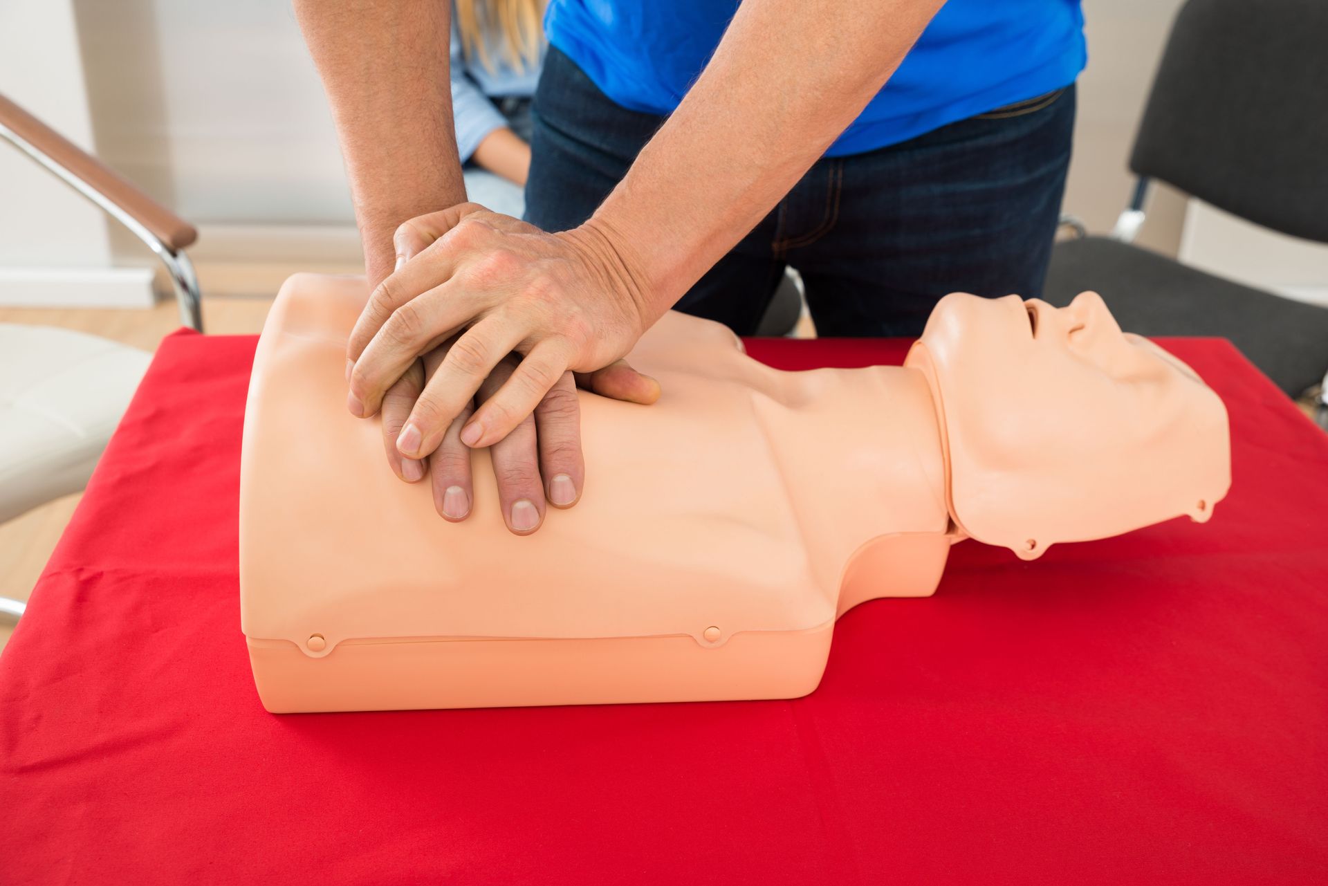 Hands performing CPR on a training mannequin on a red table.
