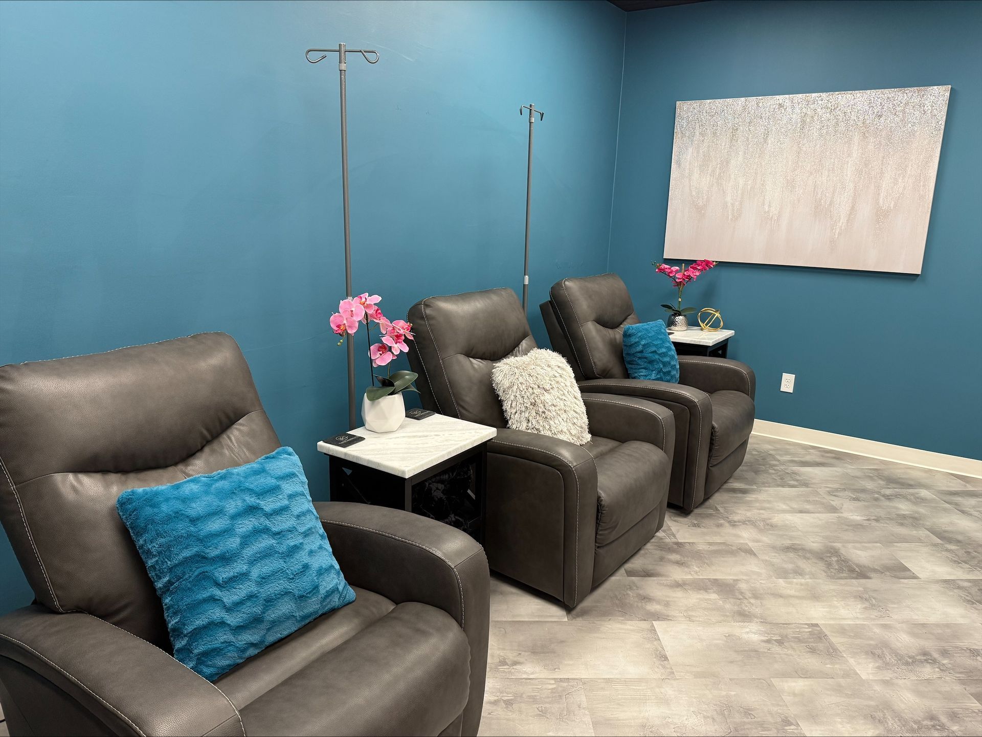 Relaxation room with IV chairs, blue wall, grey flooring, and supplies.