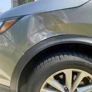 Close-up of a gray car’s front wheel and fender on a sunny day