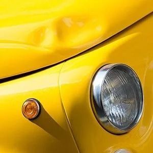 Close-up of a yellow classic car’s front headlight and amber side marker