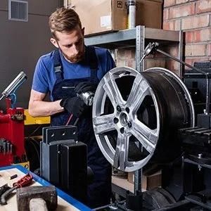 Mechanic working on a silver car wheel rim in a garage workshop
