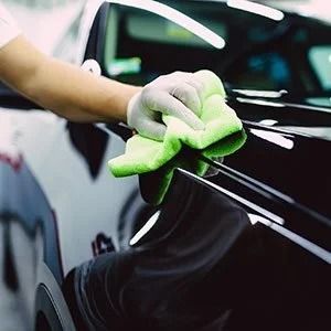 Gloved hand wiping a black car with a green microfiber cloth