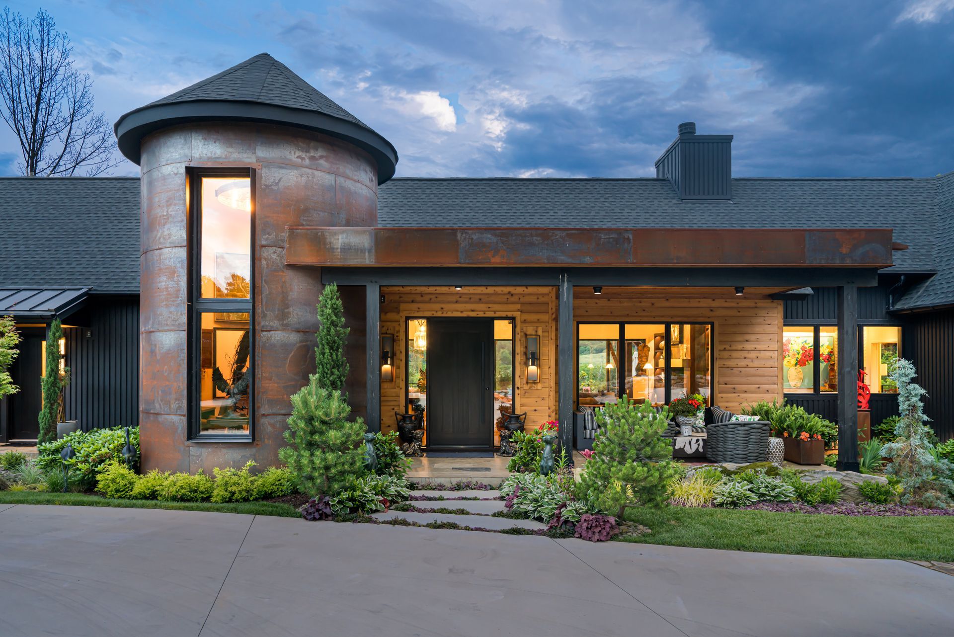 Modern brick house with a round turret, tall windows, and warm lights at dusk
