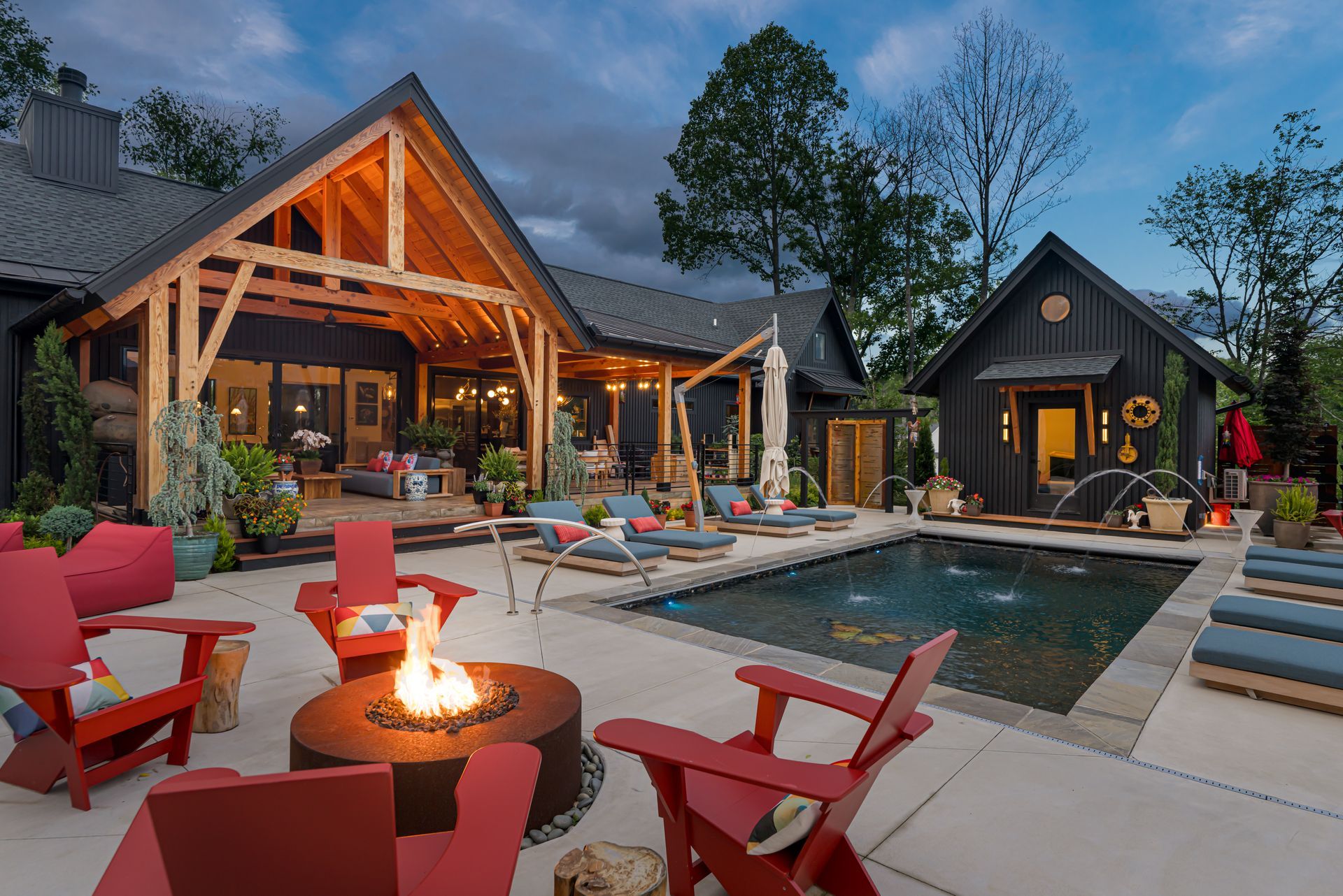 Modern cabin patio with red chairs, fire pit, and pool at dusk