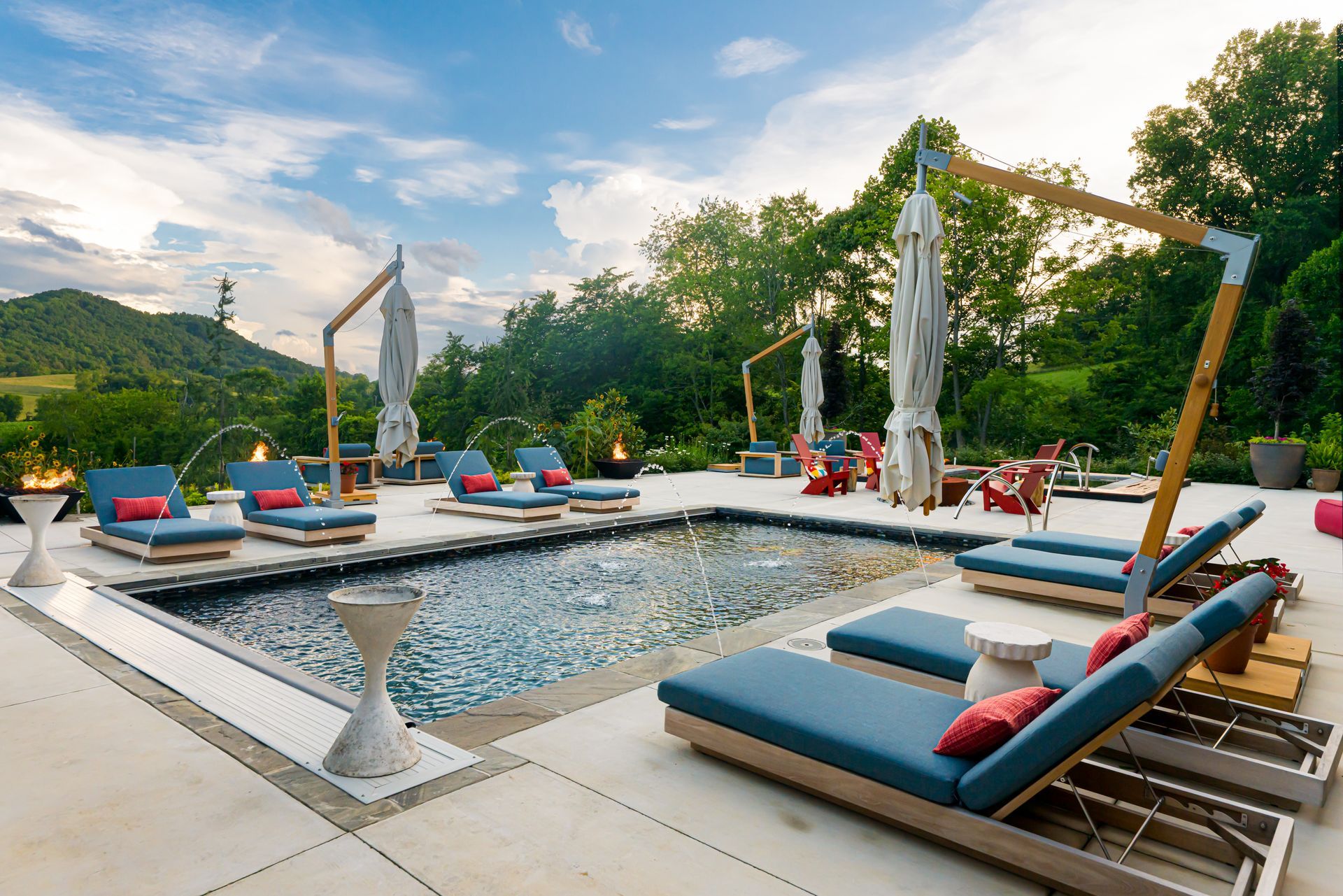 Outdoor poolside lounge with blue daybeds, white umbrellas, and mountain views at sunset