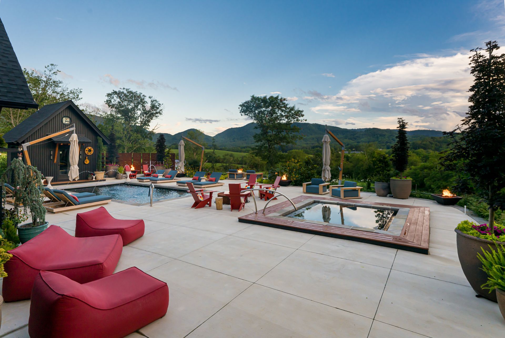 Luxury patio with red lounge chairs, hot tub, pool, and mountain views at sunset