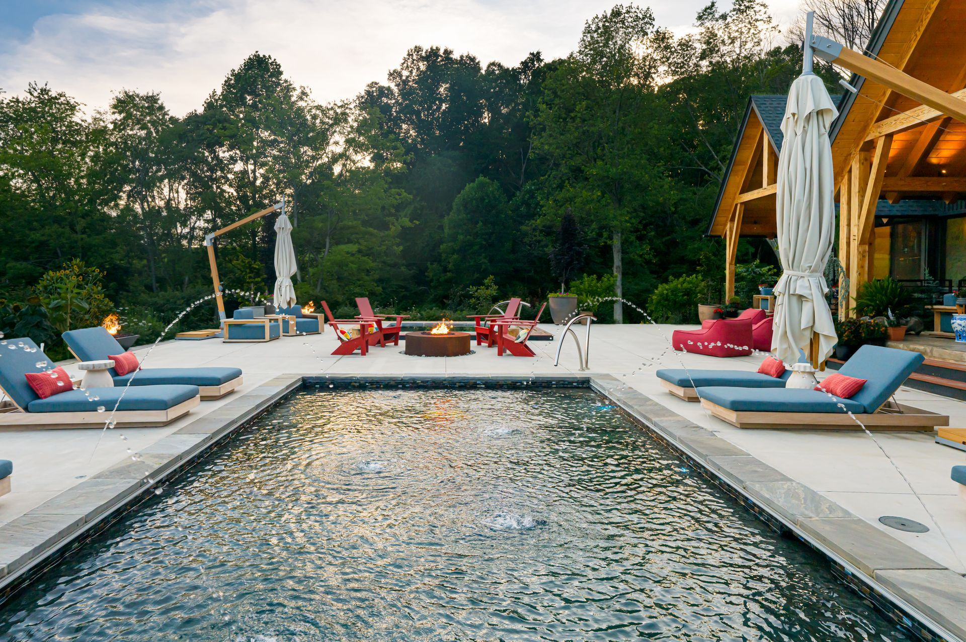 Modern poolside patio with lounge chairs, red umbrellas, and trees at sunset