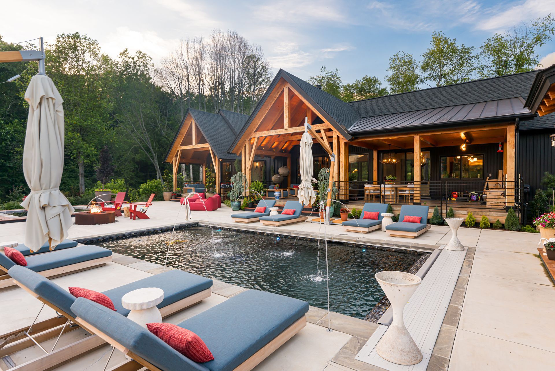 Modern outdoor pool patio with lounge chairs, cabanas, and a wooden house at sunset
