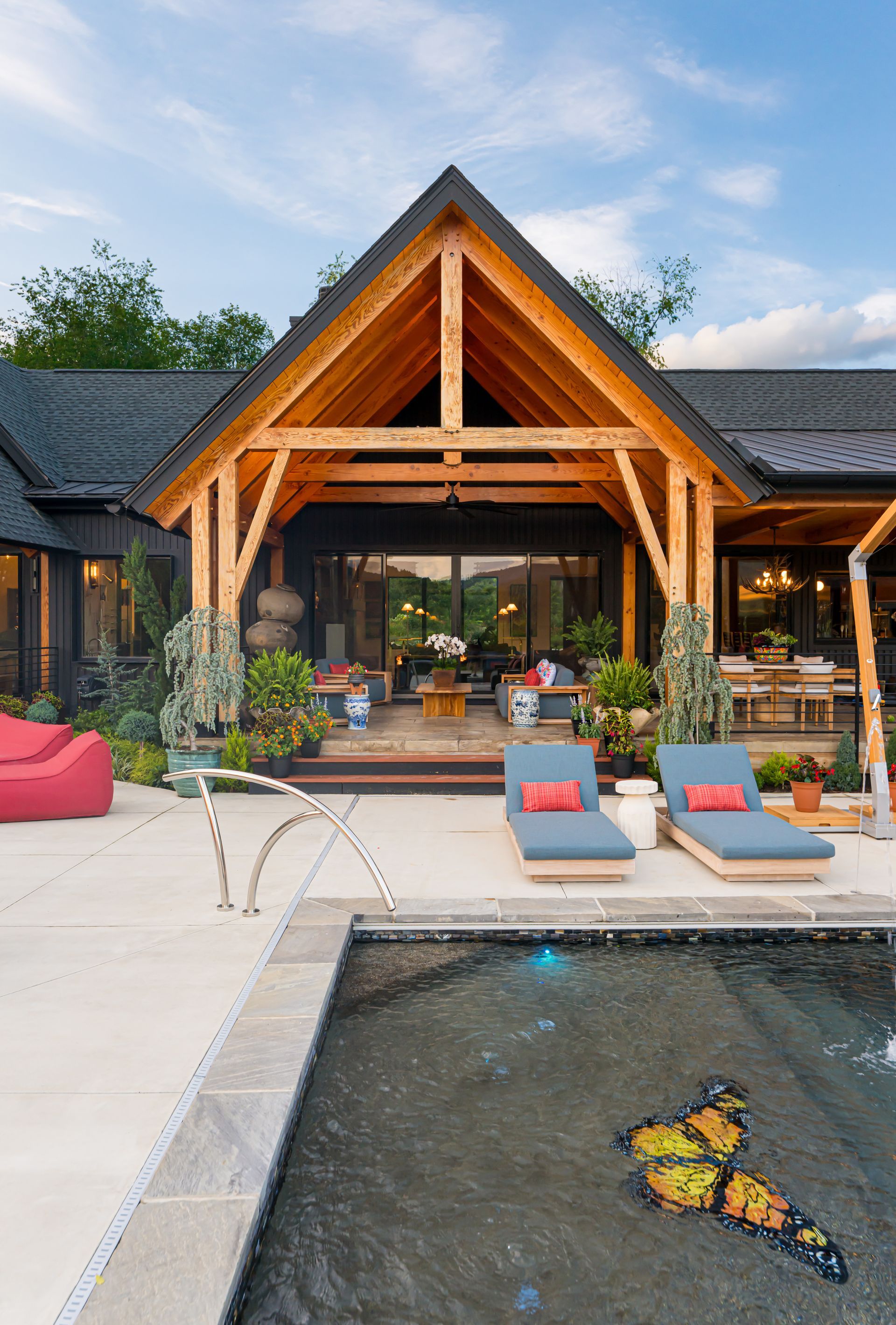 Modern house patio with wooden gable, lounge chairs, pool, and butterfly in the water