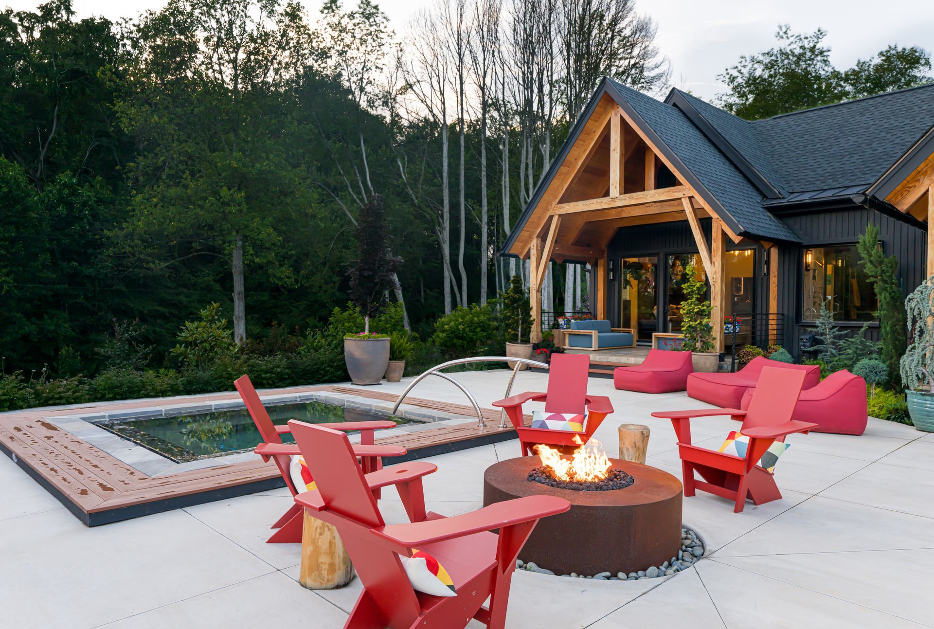 Outdoor patio with red chairs around a fire pit beside a modern wooden cabin at dusk