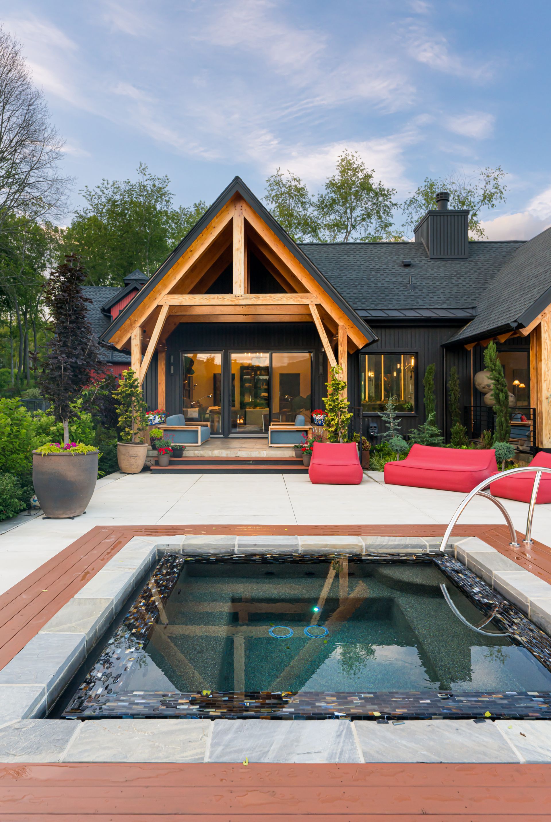 Modern house patio with a hot tub, red lounge chairs, and warm evening lighting