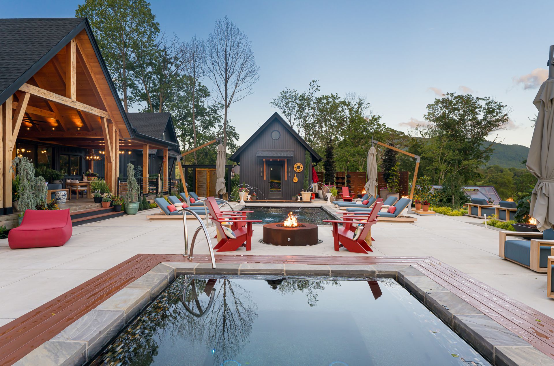 Modern outdoor patio with fire pit, red chairs, and a reflective pool at dusk