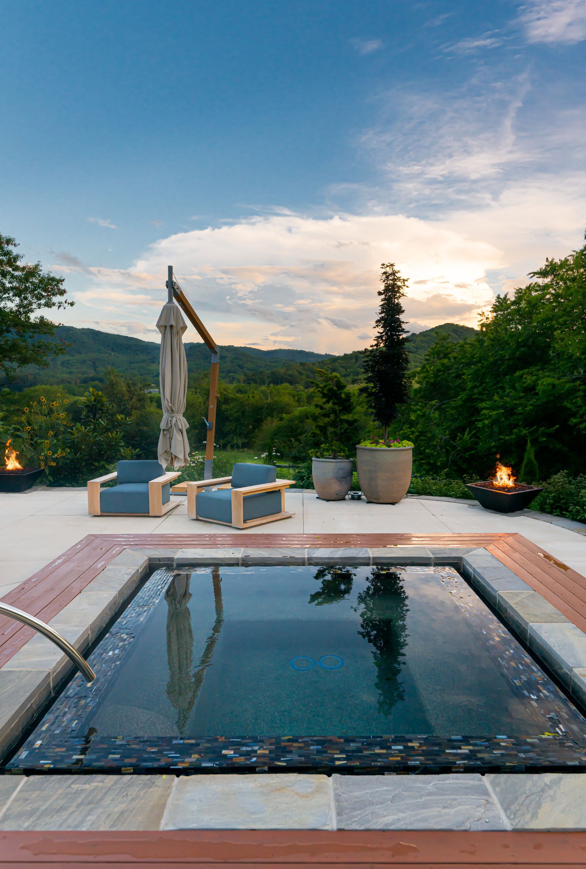 Outdoor hot tub by lounge chairs with a mountain view at sunset