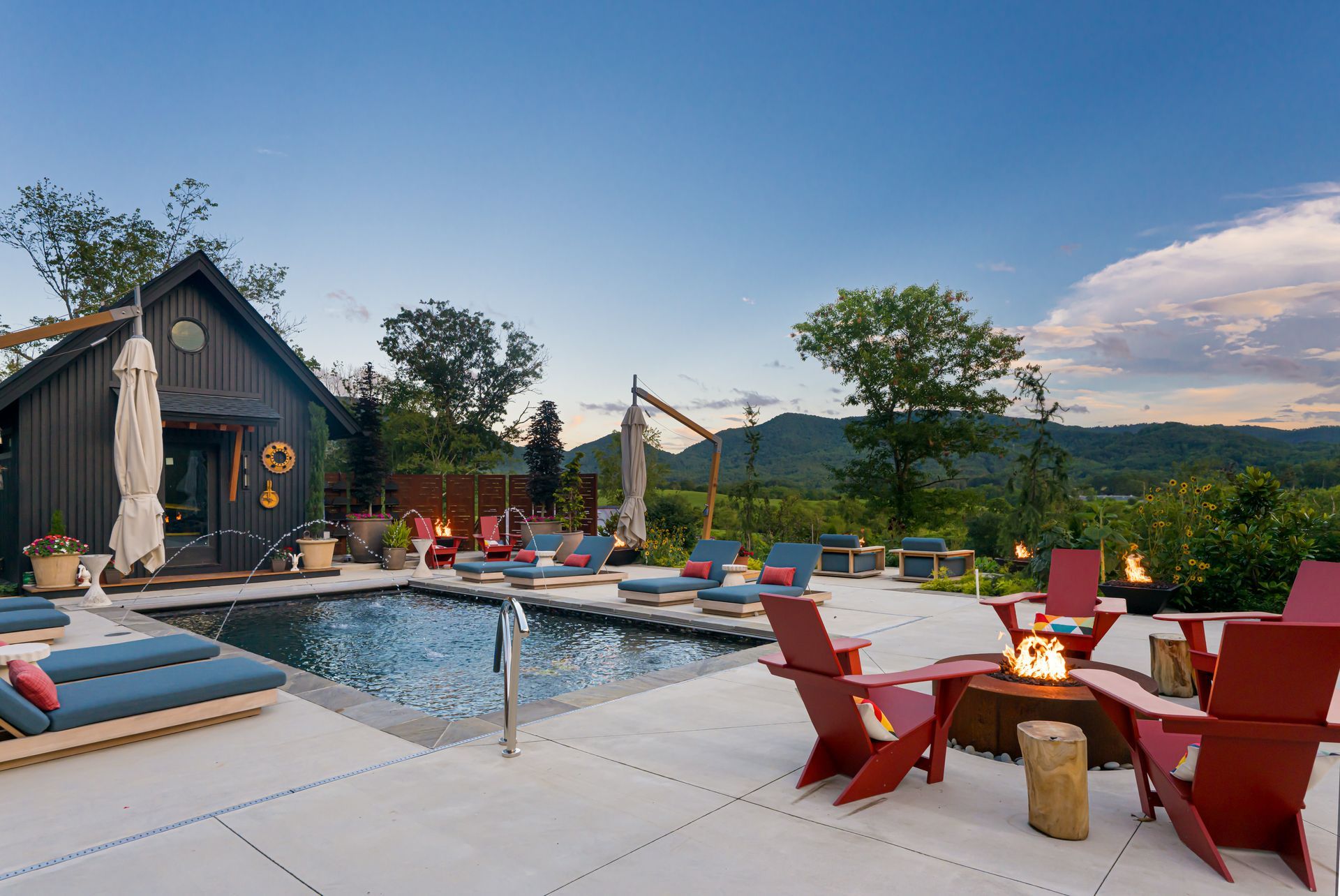 Modern poolside patio with red chairs, fire pit, lounge seating, and a mountain view at sunset
