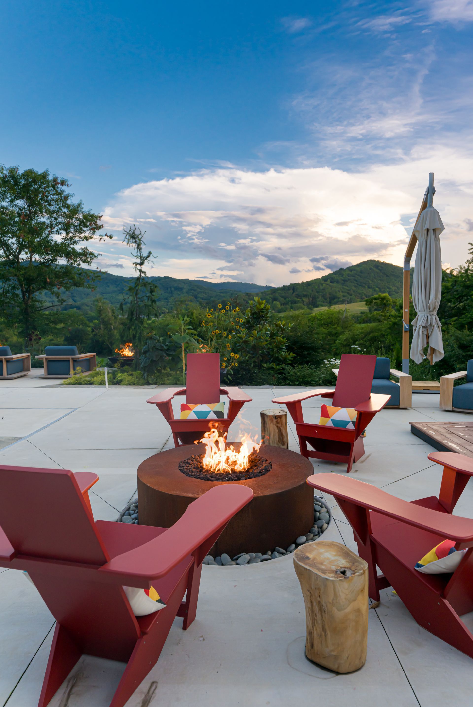Rooftop fire pit lounge with red chairs, umbrellas, and mountain sunset view