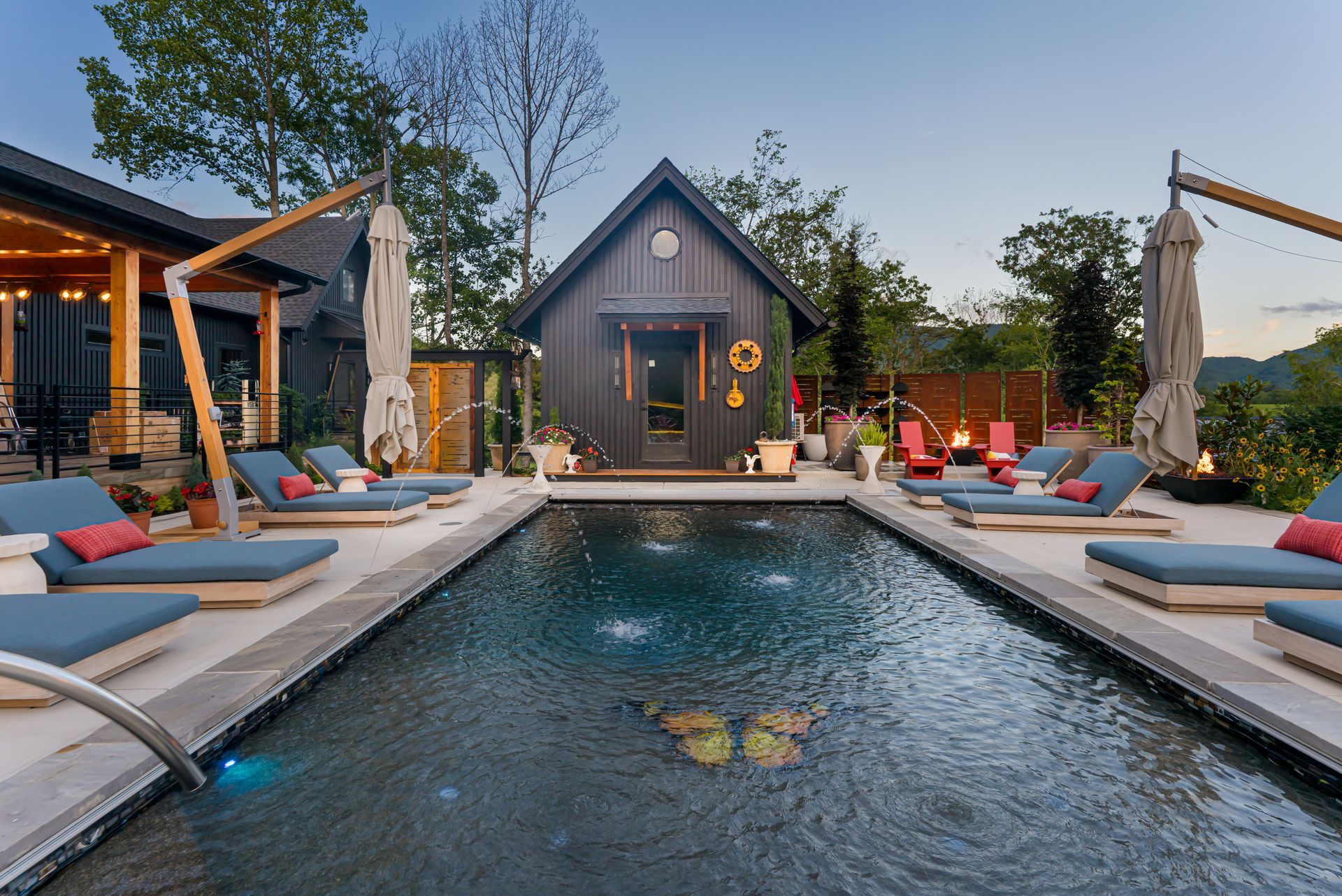 Modern poolside lounge with blue cushions, cabanas, and a small house at dusk