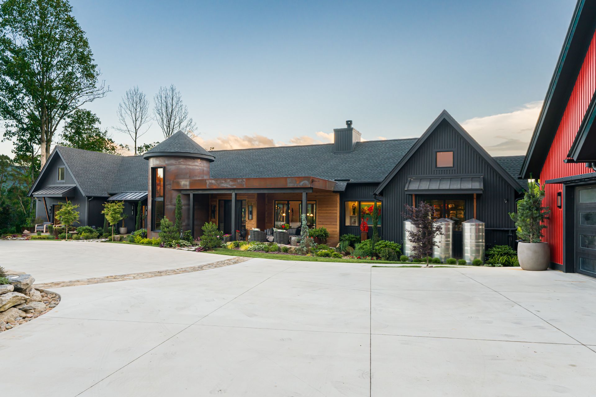 Modern ranch-style house with dark wood exterior, red garage, and wide concrete driveway under a clear sky