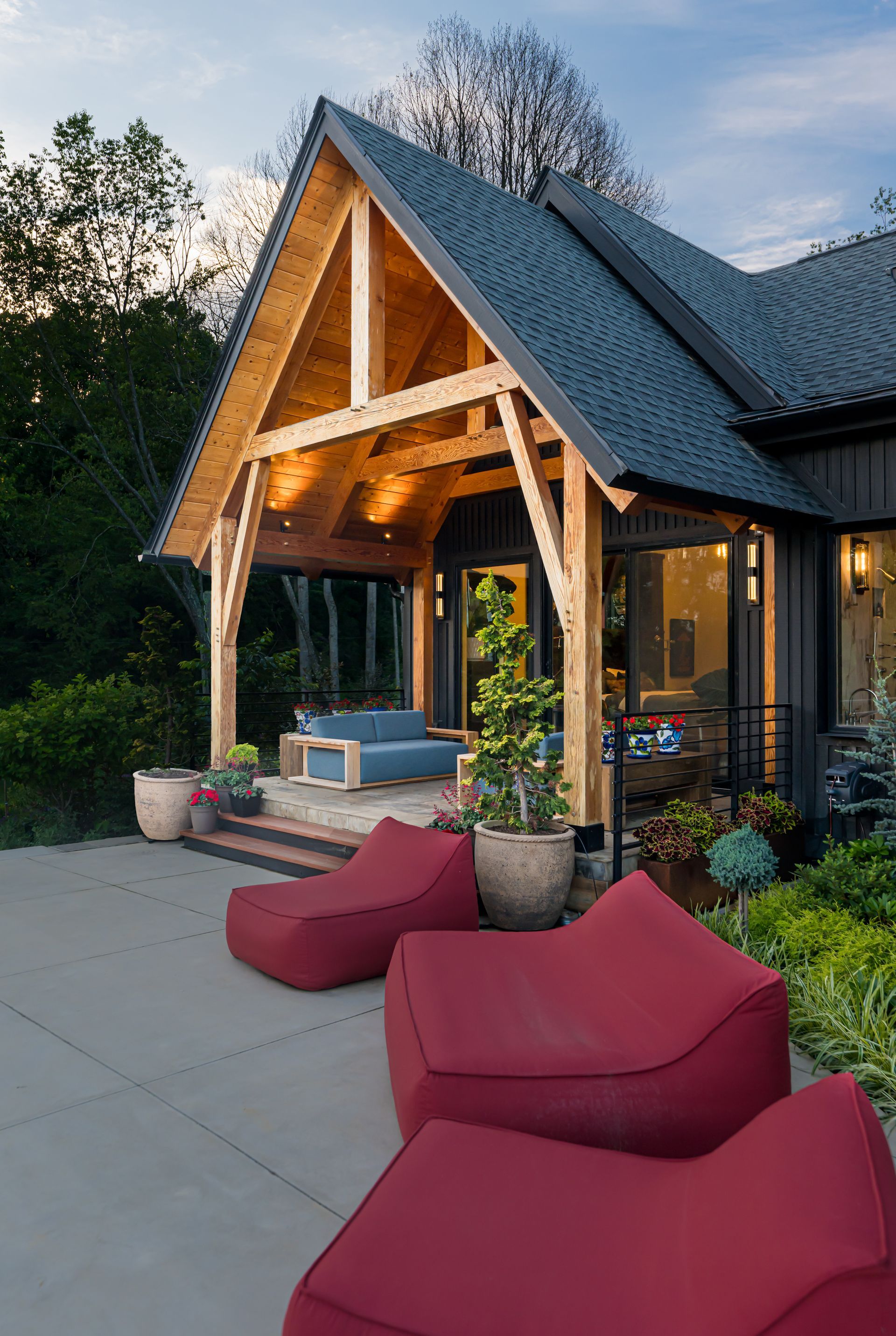 Cozy outdoor patio with red lounge chairs, blue sofa, and warm-lit wooden porch at dusk