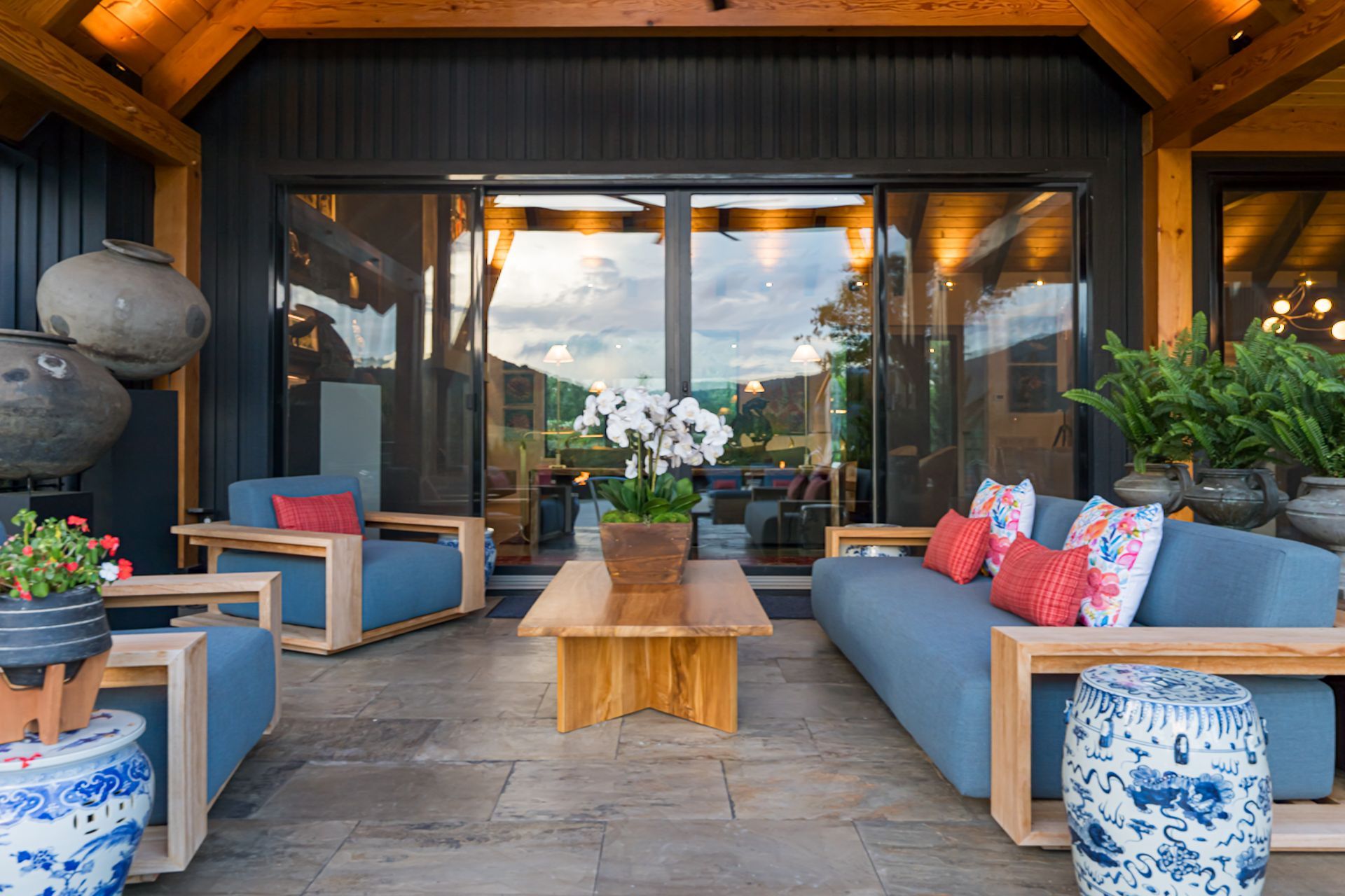 Covered patio with blue seating, wood coffee table, and potted plants in front of glass doors