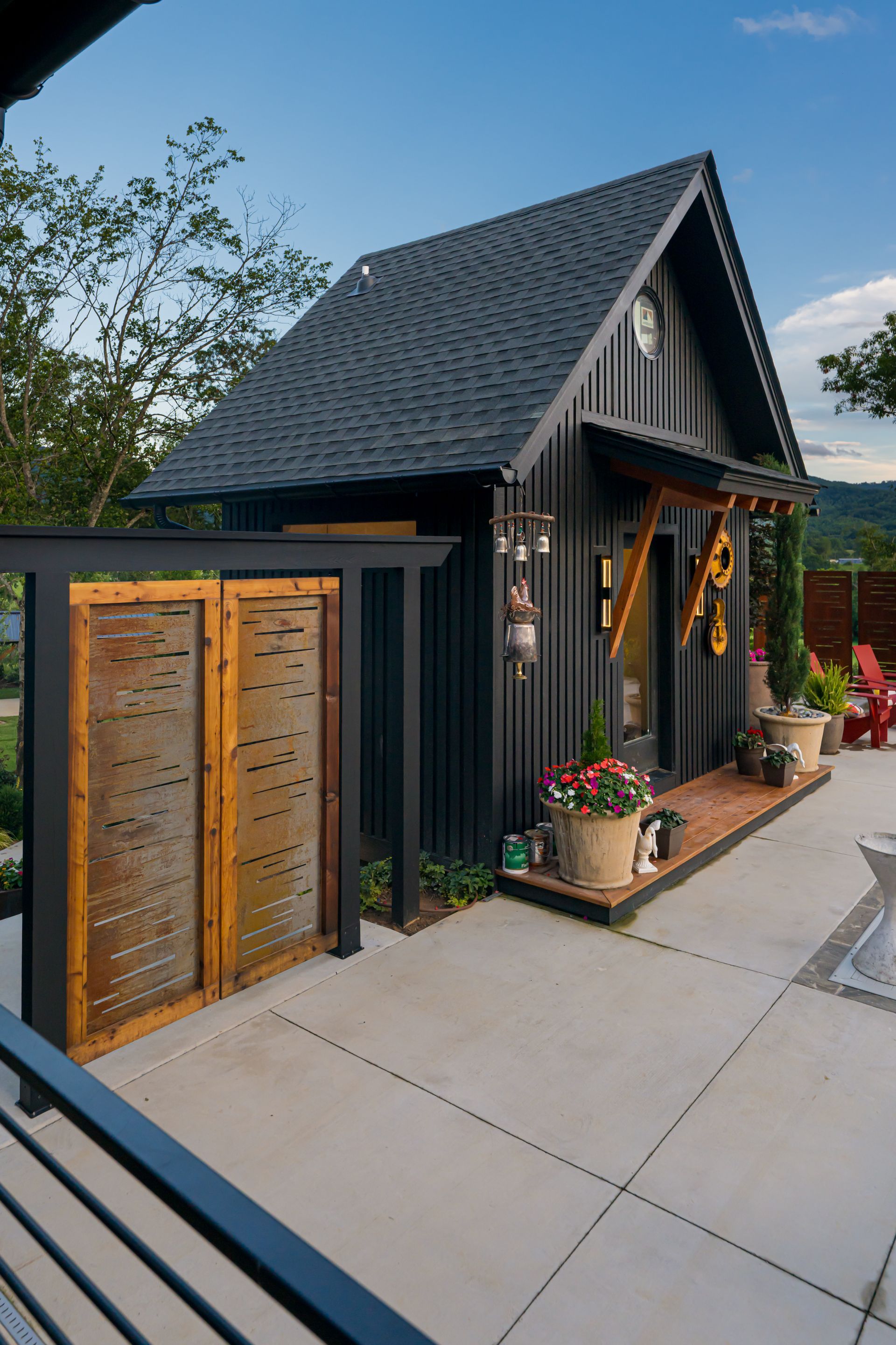 Small dark-gray house with a steep roof, wood doors, and a flower-lined front entry