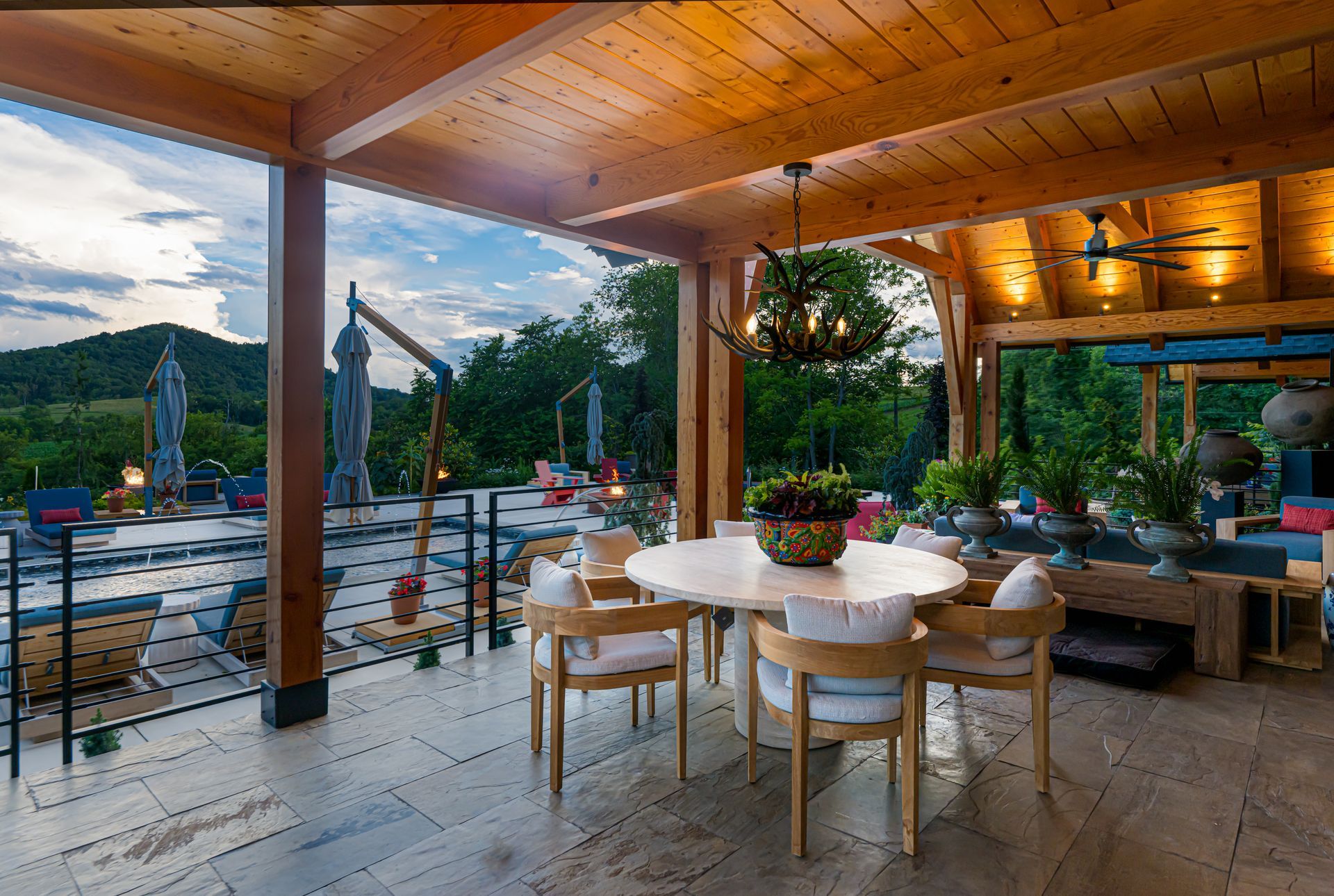 Covered outdoor patio with wooden ceiling, dining table, and poolside seating at dusk