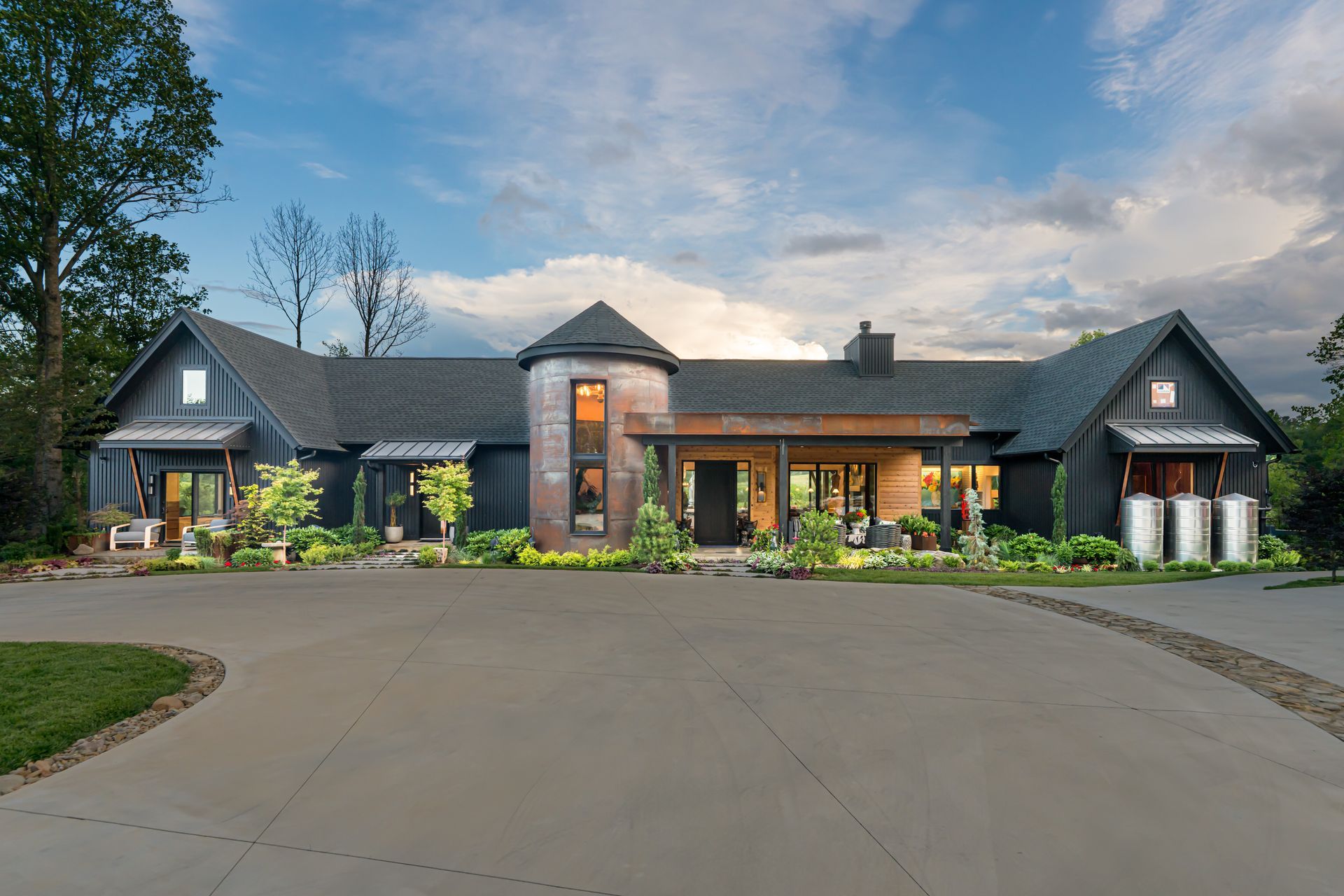 Large modern house with stone and dark wood exterior, wide driveway, and landscaped front yard at dusk