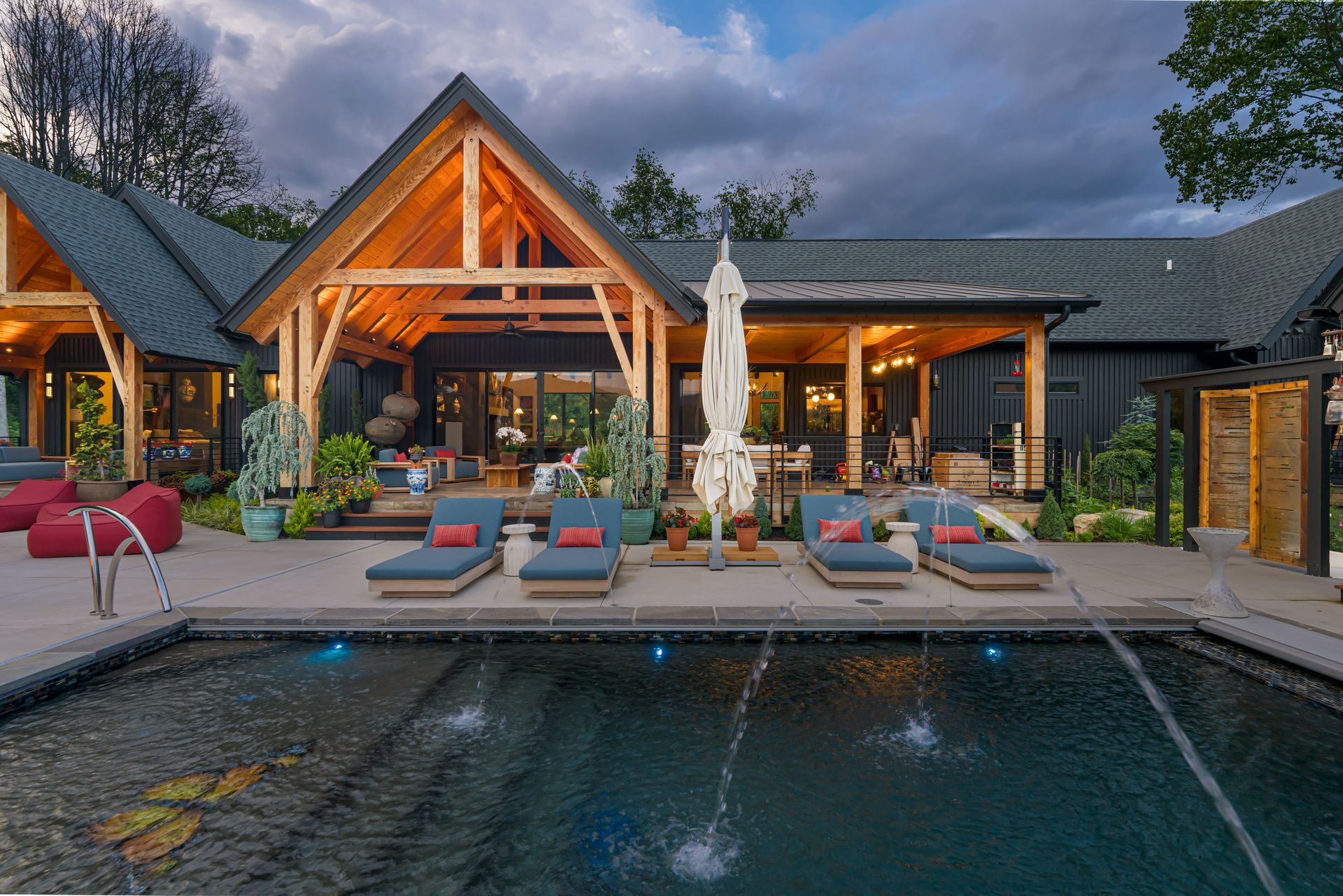 Luxury villa with lit pool deck, lounge chairs, umbrellas, and mountain view at dusk