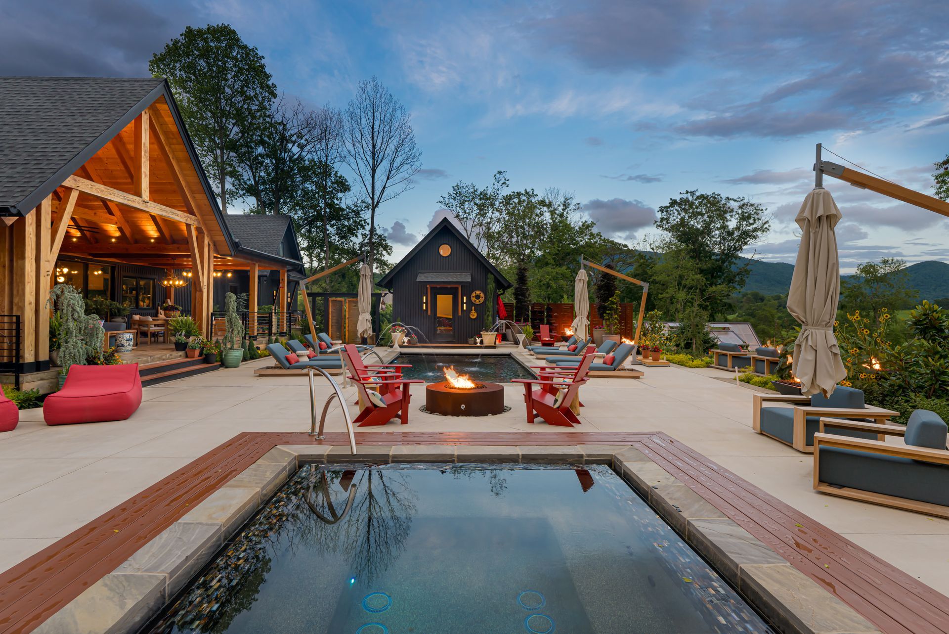 Luxury lodge patio with fire pit, hot tub, red chairs, and mountain views at dusk