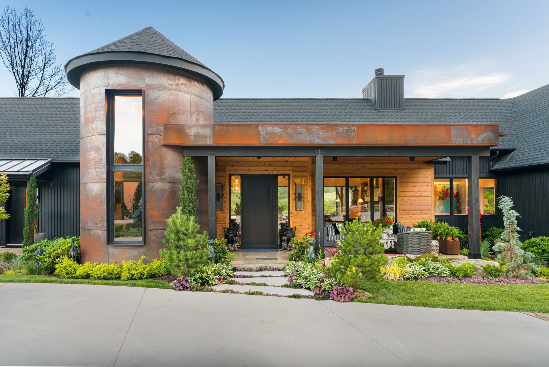 Modern brick house with a round tower, wood porch, and landscaped front yard