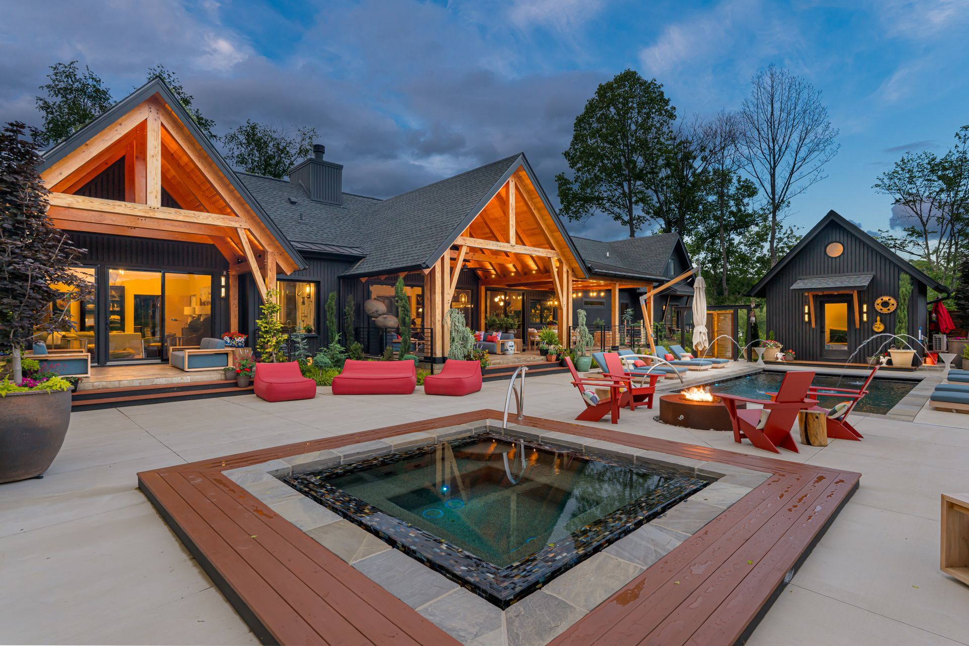 Modern lodge patio with lit wooden cabins, red seating, and a square fire pit at dusk