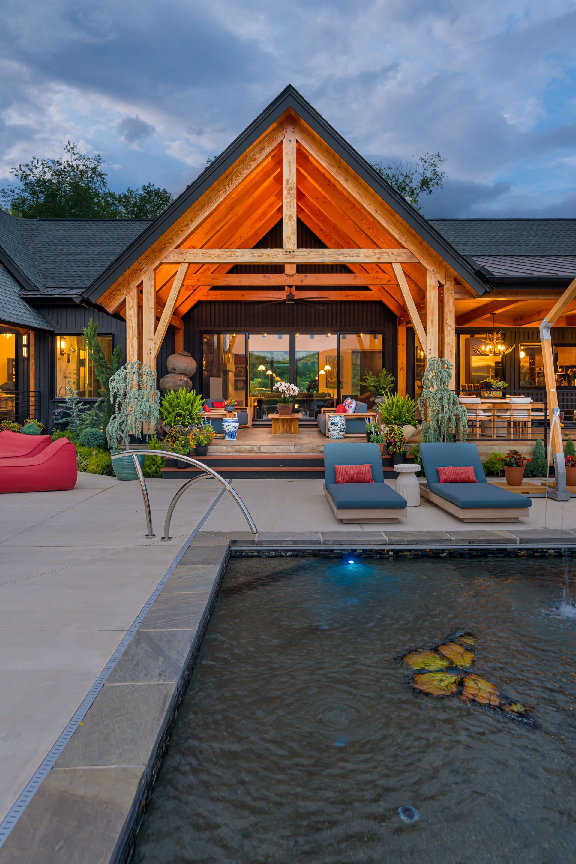 Luxury lodge courtyard with a lit wooden gable, lounge chairs, and a reflecting pool at dusk