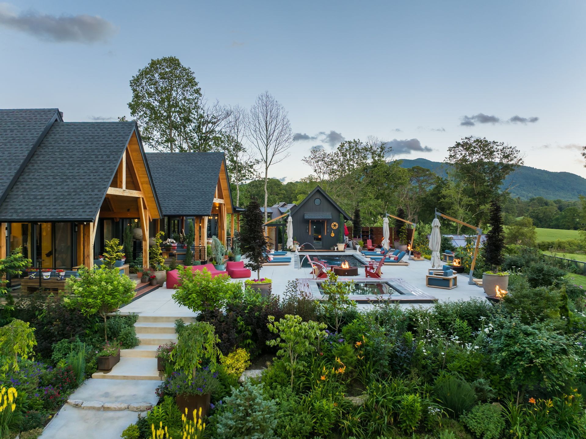 Resort cottages and pool with colorful flowers, surrounded by green hills and mountains under a clear sky