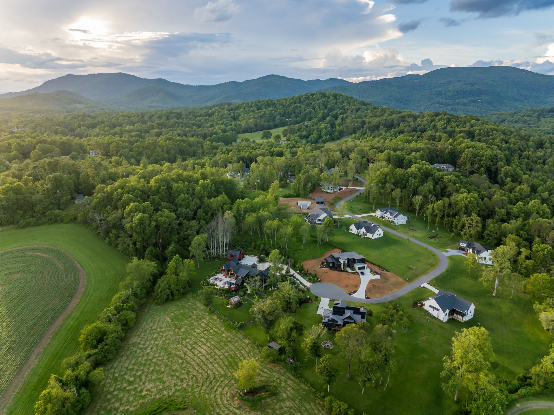Aerial view of a rural farmstead with houses, fields, and forested mountains at sunset.